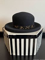 Front view of black wool felt bowler hat on hexagonal striped hat box