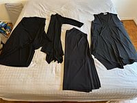 Four black garments on bed: tabard top and three dresses