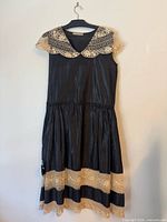 Front view of black sleeveless dress with lace collar and hem