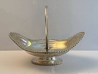 Side profile of sterling basket showing swing handle, pedestal base and beaded rim