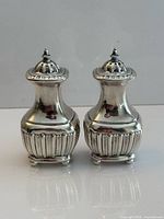 Front view of both sterling silver pepper shakers standing side by side