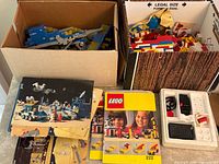 Two boxes of loose LEGO pieces with several instruction manuals on tabletop