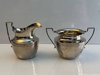 Front view of sterling silver cream pitcher and sugar pot