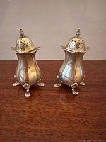 Front view of both sterling shakers showing pot-bellied form, lion-paw feet, and domed pierced tops