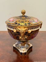 Full view of porcelain pot-pourri bowl with lid showing cobalt ground, gilt decoration, ram mask handles and pedestal base.