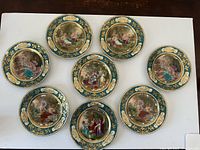 Eight hand-painted plates showing romantic scenes on jade green and gold ground