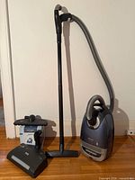 Vacuum canister, wand, hose, floorhead and powerbrush displayed against wall