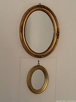 Two oval gilt mirrors hung on wall showing size difference