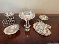 Group shot of several silver-plated items including pedestal stand, sauce boat with plate, small bowl, bottle stand, toast rack