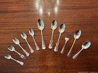 Group of 11 sterling silver spoons and one fork arranged on wood surface