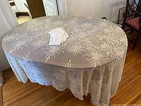 Full view of lace tablecloth draped on oval table with placemats stacked