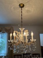 Full view of six-arm glass chandelier hanging from chain with bulbs lit
