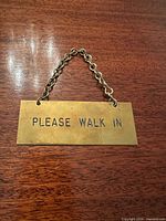 Front view of brass door sign showing etched text and hanging chain