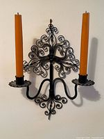 Front view of wrought iron double candle wall sconce with two orange taper candles mounted on wall
