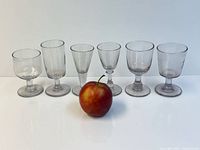 Front view of six hand-blown stemmed glasses with apple for scale