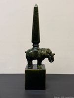 Full view of green glazed ceramic elephant obelisk sculpture on black surface