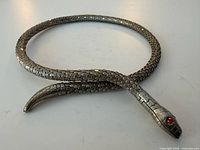 Full view of coiled snake mesh necklace showing head, tail and scale texture