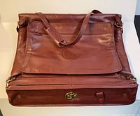 Full view of burgundy leather garment bag with strap and front pocket