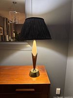Full view of lamp lit, showing teak and brass body, pleated black shade, brass base