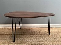 Overall view of tripod coffee table showing kidney-shaped wood-tone top and three metal hairpin legs