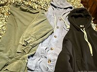 Three sweatshirts laid out: green crewneck, blue waffle shacket, black hoodie