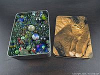 Open tin filled with assorted marbles beside lid