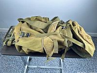 Side view of olive drab canvas rucksack on table showing webbing straps and external frame corner