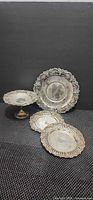 Group view of four silver-plated pieces including pedestal compote and three plates