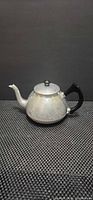 Side view of engraved metal teapot with black handle and lid