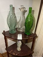 Four glass fish bottles on a small shelving unit