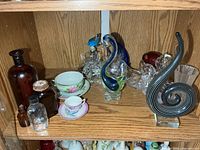 Shelf containing art-glass sculptures, teacups, crystal pieces, bottles
