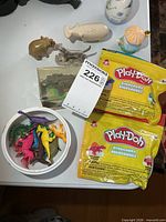 All items overview: Play-Doh kits, plastic dinosaurs in bowl, stone and metal animal figurines, ceramic pieces