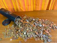 Coins spilling from black tube onto table showing variety of pennies