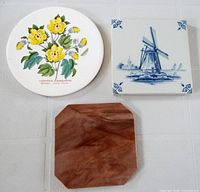 Group shot of three trivets: square blue Delft windmill, round floral cotton, octagonal brown marble