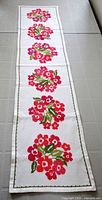 Full view of white table runner showing five repeated floral motifs and green border