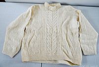 Front view of cream hand-knit wool sweater showing cable and textured pattern