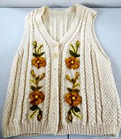 Full front view of cream wool cable knit vest with floral embroidery and buttons