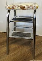 Full side view showing padded triangular seat, chrome legs, two steps