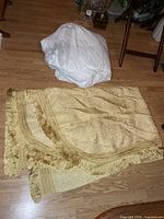 Gold fringed bedspread folded beside white mattress protector on floor