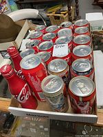 Tray showing multiple empty Coca-Cola cans and two aluminum bottles