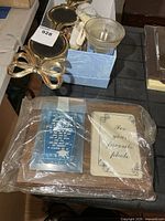Lot overview showing gold-tone metal frame, box with mugs, glass dish, doll, and sealed graduation plaque