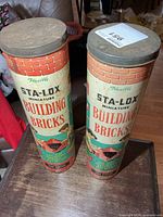 Two Sta-Lox building bricks cans standing upright with lids