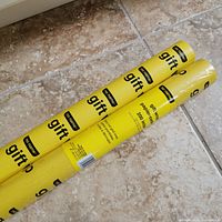 Two yellow No Name gift-wrap rolls on tile floor