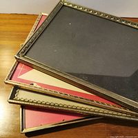 Stack of four brass-tone metal frames showing glass fronts and decorative edges