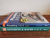 Spine view of both hardcover books stacked: Plumbing 1-2-3 on top, Kitchens & Baths 1-2-3 below