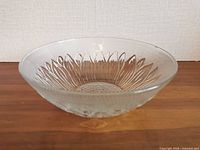 Side view of clear pressed glass bowl showing sunflower relief