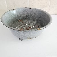 Top view of gray spatter graniteware pan showing interior perforations and chipped enamel