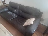 Front angled view of black leather sofa with pillow