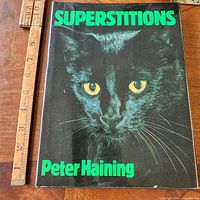 Front dust-jacketed cover of Superstitions book beside ruler for scale