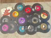 Assorted 45 RPM singles spread on carpet with one paper sleeve